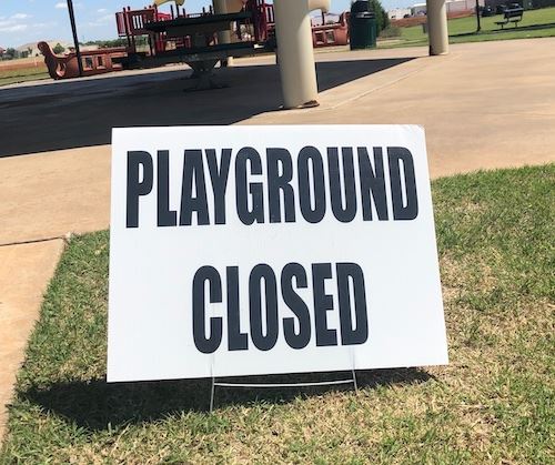 A sign in grass next to a pavilion that says Playground Closed